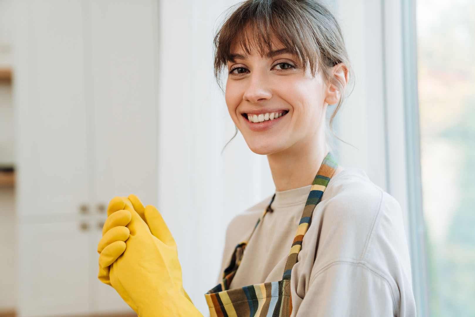 White young woman in apron smiling while doing housework